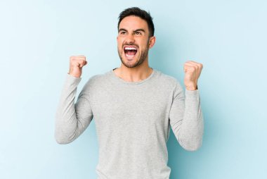Mavi arka planda izole edilmiş genç beyaz bir adam zaferden sonra yumruğunu kaldırıyor, kazanan konsept..