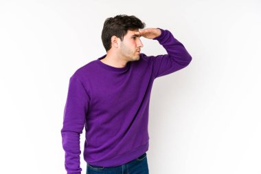 Genç adam beyaz arka planda izole edilmiş. Uzağa bakıyor. Elini alnına koyuyor..