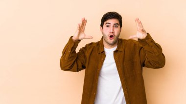 Bir zaferi ya da başarıyı kutlayan bej arka plandaki genç adam şaşırmış ve şok olmuştu..