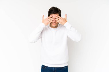 Beyaz arka planda izole edilmiş genç adam elleriyle gözlerini kapatmaktan korkuyor..