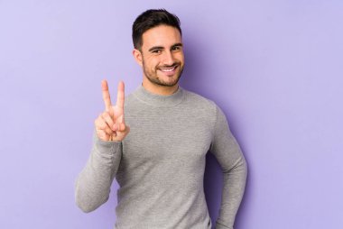 Mor arka planda izole edilmiş genç beyaz adam iki numarayı parmaklarıyla gösteriyor..