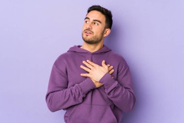 Mor arka planda izole edilmiş beyaz bir genç, dost bir ifadeye sahip, avuçlarını göğsüne bastırıyor. Aşk konsepti.