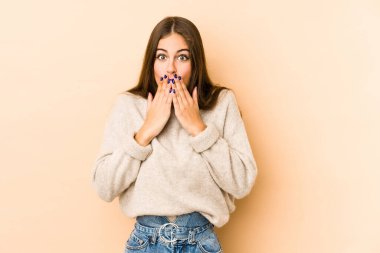 Beyazlı genç bir kadın bej arka planda izole edildi. Elleriyle ağzını kapatırken şok oldu..