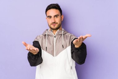 Mor arka planda izole genç beyaz adam kollarıyla ölçek yapar, mutlu ve kendinden emin hisseder..