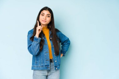 Mavi arka planda izole edilmiş genç Hintli kadın bir numarayı parmağıyla gösteriyor..