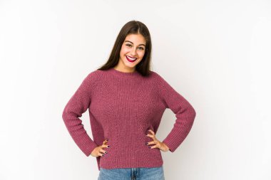 Beyaz arka planda izole edilmiş beyaz tenli genç bir kadın ellerini kalçasından ayırmıyor..