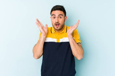 Kafkasyalı genç adam mavi arka planda izole edildi. Şaşırdı ve şok oldu..