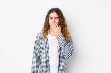 Genç, uzun saçlı adam, esneme pozu veriyor. Elle ağzını kapatan yorgun bir hareket sergiliyor..