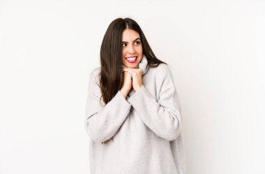 Beyaz bir arka planda izole edilmiş genç beyaz kadın ellerini çenesinin altında tutuyor, mutlu bir şekilde yana bakıyor..