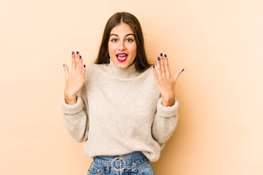 Beyazlı genç bir kadın bej arka planda izole edilmiş. 10 numarayı elleriyle gösteriyor..
