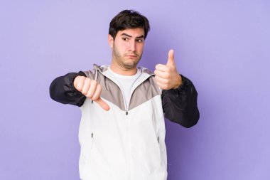 Mor arka planda izole edilmiş genç adam, baş parmağını kaldırıyor, zor bir seçim konsepti.