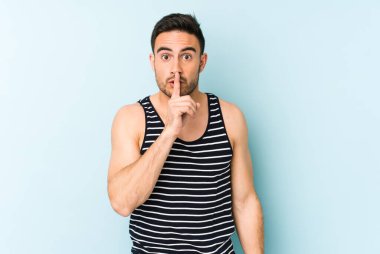 Mavi arka planda izole edilmiş genç beyaz bir adam ya sır saklıyor ya da sessizlik istiyor..