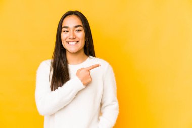 Sarı arka planda izole edilmiş genç bir kadın gülümsüyor ve boş alanda bir şeyler gösteriyor..