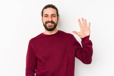 Genç, uzun saçlı bir adam beyaz bir arka planda izole edilmiş. Gülümsüyor. Beş numarayı parmaklarıyla gösteriyor..