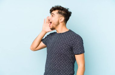 Mavi bir arka planda izole edilmiş genç bir Arap bağırıyor ve avuç içini açık tutuyor..