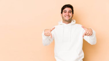 Bej arka planda izole edilmiş genç adam parmakları aşağıda, olumlu hisler içinde..