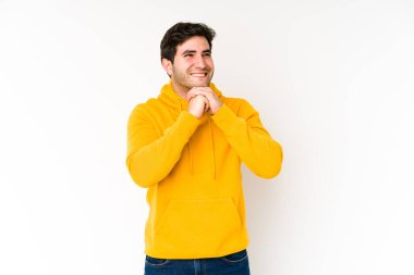 Beyaz arka planda izole genç adam ellerini çenesinin altında tutuyor, mutlu bir şekilde yan tarafa bakıyor..