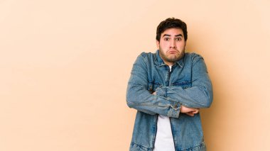 Bej arka planda izole edilmiş genç adam omuz silkiyor ve gözleri açık..