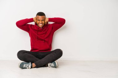 Genç latin adam yerde tek başına oturmuş kulakları kulaklarıyla kapatıyor ve çok fazla ses duymamaya çalışıyor..