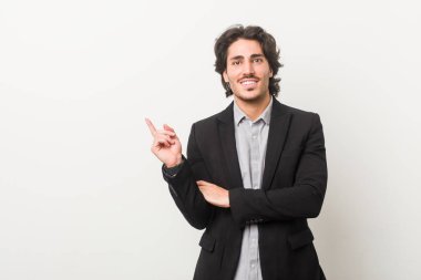 Genç bir iş adamı beyaz bir arkaplanda gülümseyerek işaret parmağıyla işaret ediyor..