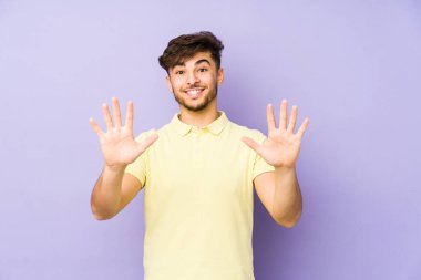 Mor arka planda izole edilmiş genç bir Arap adam on numarayı elleriyle gösteriyor..