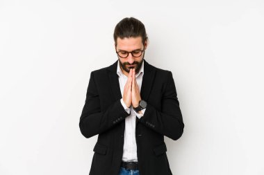 Beyaz bir arka planda izole edilmiş beyaz tenli genç bir iş adamı el ele dua ederken, kendine güveniyor..