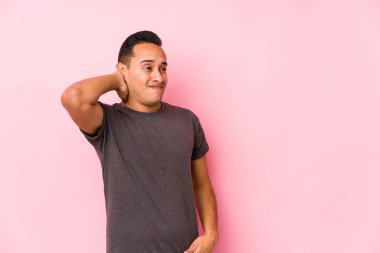 Pembe arka planda poz veren Latin bir adam kafasının arkasına dokunuyor, düşünüyor ve bir seçim yapıyor..