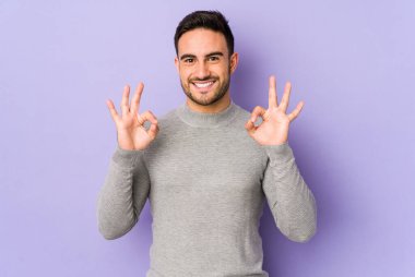 Genç beyaz adam mor arka planda izole edilmiş neşeli ve kendinden emin, iyi bir jest yapıyor..