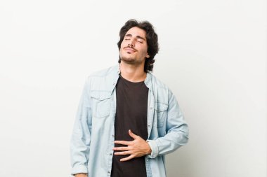 Beyaz arka planda genç yakışıklı bir adam karnına dokunur, nazikçe gülümser, yemek yer ve tatmin olur..