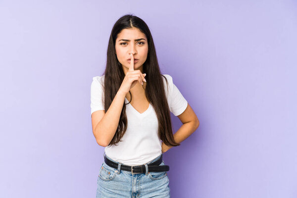 Young indian woman isolated on purple background keeping a secret or asking for silence.