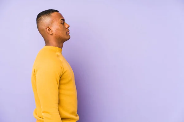 Young latin man isolated on purple background gazing left, sideways pose.