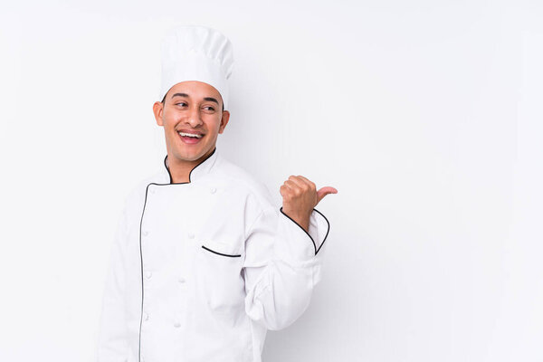 Young latin chef man isolated points with thumb finger away, laughing and carefree.