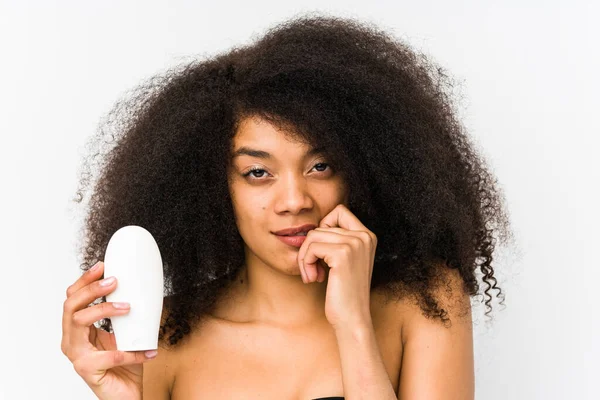 Mujer Afro Joven Sosteniendo Una Crema Hidratante Aislada Mordiendo Las — Foto de Stock