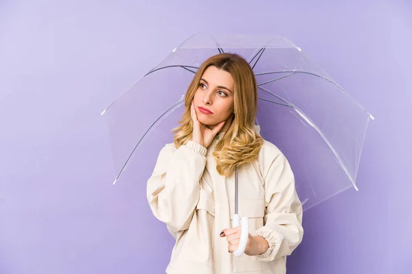 Young blonde woman holding an umbrella isolated Young blonde woman holding an umbrella isolated looking sideways with doubtful and skeptical expression.