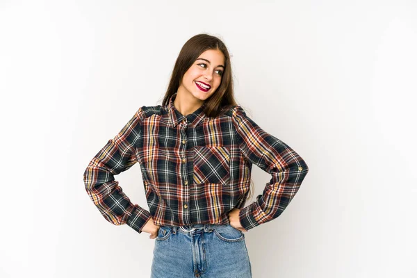 Beyaz arka planda izole edilmiş beyaz tenli genç bir kadın ellerini kalçasından ayırmıyor..