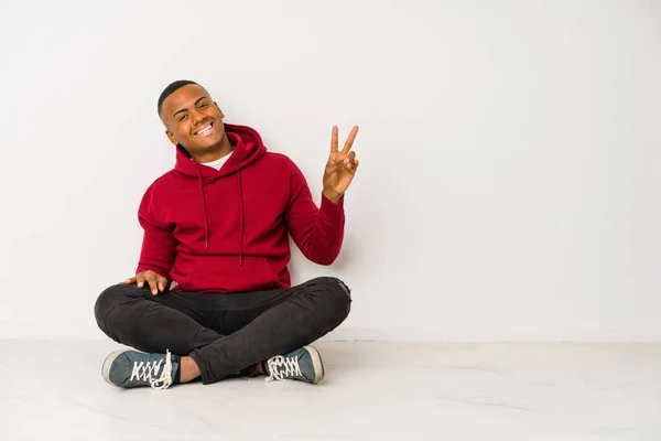 年轻的拉丁裔男子坐在地板上 孤独而快乐 无忧无虑 用手指展示着和平的象征 — 图库照片