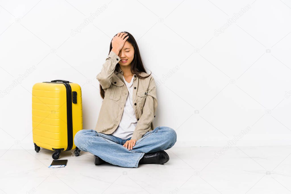 Young chinese traveler woman sitting holding a boarding passes forgetting something, slapping forehead with palm and closing eyes.