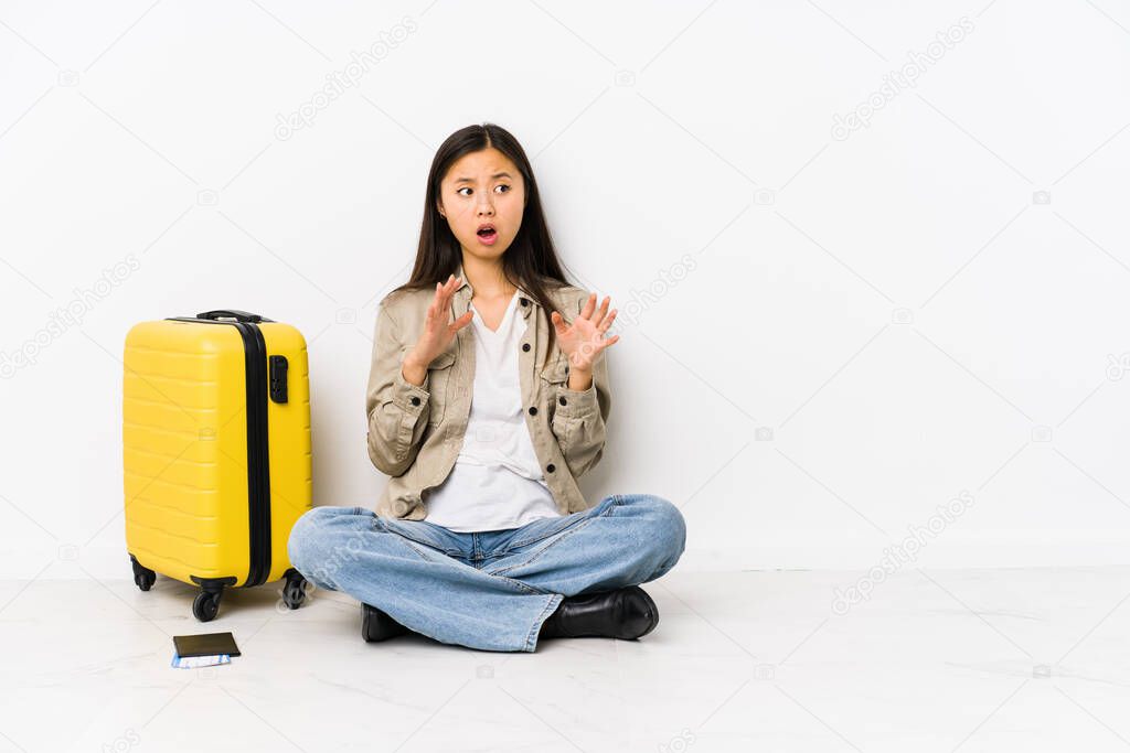 Young chinese traveler woman sitting holding a boarding passes being shocked due to an imminent danger