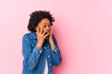Genç Afrikalı Amerikalı bir kadın pembe bir arka plana karşı yüksek sesle bağırıyor, gözleri açık ve elleri gergin tutuyor..