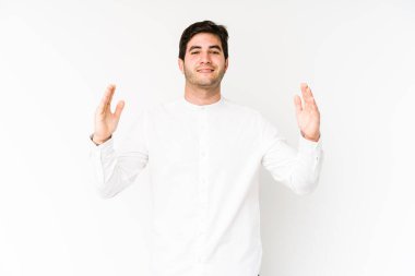 Beyaz arka planda izole edilmiş genç bir adam işaret parmaklarıyla küçük bir şey tutuyor, gülümsüyor ve kendinden emin..