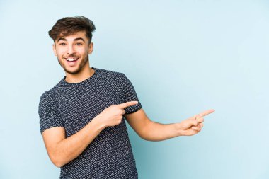 Mavi bir arka planda izole edilmiş genç bir Arap işaret parmaklarıyla işaret ederek heyecanlanıyor..