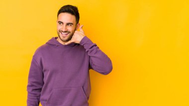 Sarı fırında izole edilmiş genç beyaz bir adam parmaklarıyla bir cep telefonu hareketi gösteriyor..