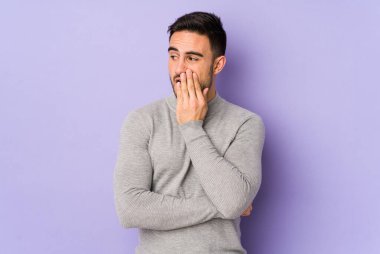 Mor arka planda izole edilmiş genç beyaz adam esniyor. Ağzı eliyle kapatan yorgun bir hareket sergiliyor..