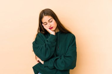 Beyaz tenli genç bir kadın bej arka planda izole edilmiş. Sıkılmış, yorgun ve dinlenmeye ihtiyacı var..