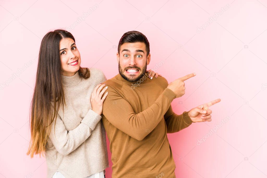 Young caucasian couple isolated shocked pointing with index fingers to a copy space.