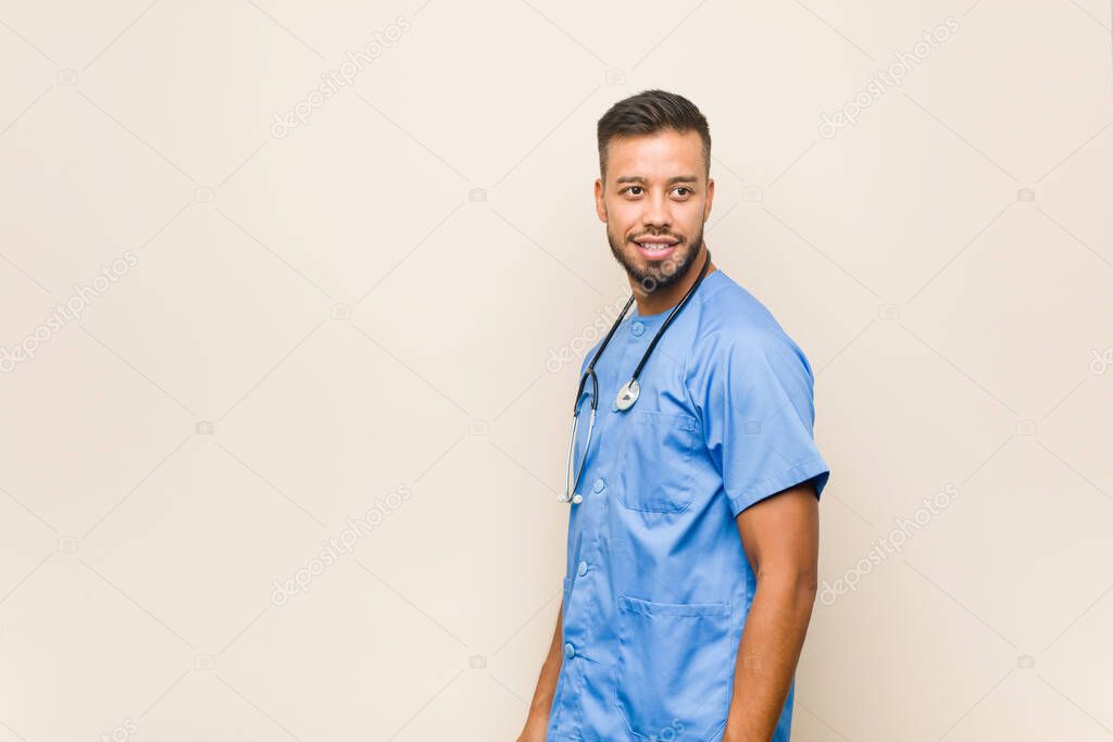 Young south-asian nurse man looks aside smiling, cheerful and pleasant.