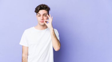 Mor arka planda izole edilmiş genç, beyaz bir adam dudaklarında parmaklarıyla bir sır saklıyor..