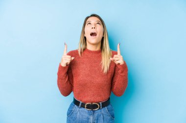 Kafkasyalı genç bir kadın yalnız poz verip ağzı açık bir şekilde yukarı işaret ediyor..