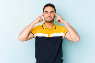 Kafkasyalı genç adam mavi arka planda izole edilmiş bir göreve odaklanmış, parmaklarını işaret ediyor..