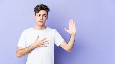 Mor arka planda izole edilmiş genç beyaz adam yemin ediyor, elini göğsüne koyuyor..
